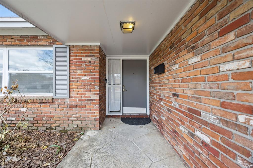 A brick-walled entryway features a gray front door with a side window and light — 2504 LAUDERDALE COURT, ORLANDO, FL