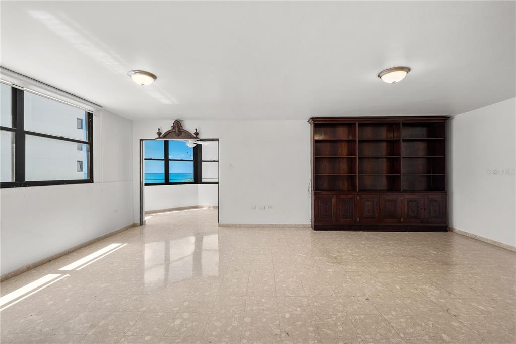 A spacious room with tile flooring, a large built-in wooden bookcase, and an ocean view — 2 WASHINGTON STREET UNIT 204, SAN JUAN, PR