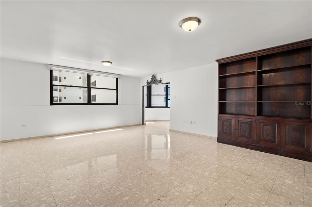 A bright, empty living room features light tile flooring, white walls, and a large wooden bookshelf — 2 WASHINGTON STREET UNIT 204, SAN JUAN, PR