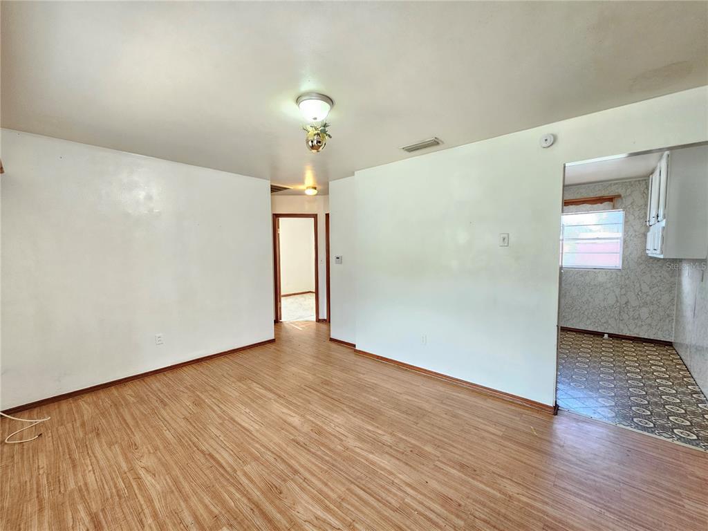 An interior view shows a living area with wood-look flooring, white walls, and a kitchen — 2302 BURNS STREET, LAKELAND, FL