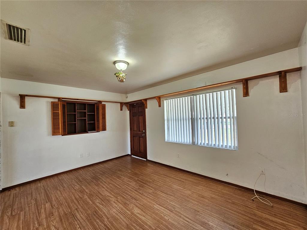 An empty room features wood-look flooring, white walls, a window with blinds, and wooden shelving — 2302 BURNS STREET, LAKELAND, FL