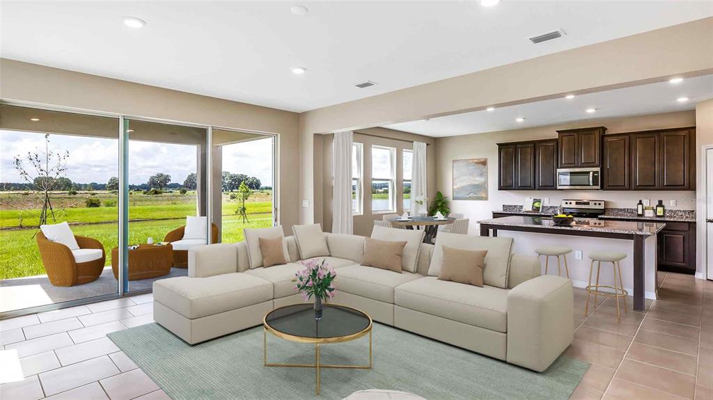 This open-concept living room and kitchen features a large sectional, sliding glass doors, and tile flooring — 32679 DULUTH DRIVE, WESLEY CHAPEL, FL