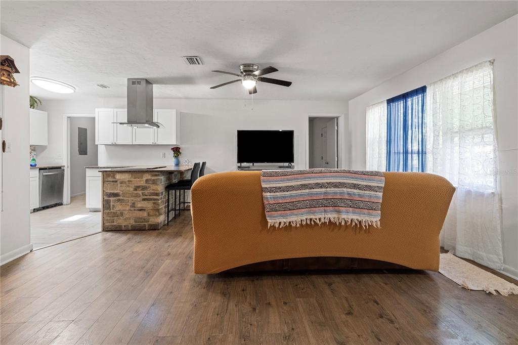 A living room with wood-look flooring, a stone-faced kitchen island, and a sofa facing a television — 1009 SE 20TH STREET, GAINESVILLE, FL