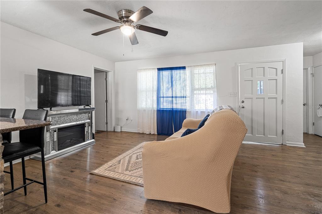 A living room features wood-look flooring, a ceiling fan, a sofa, and a fireplace console — 1009 SE 20TH STREET, GAINESVILLE, FL