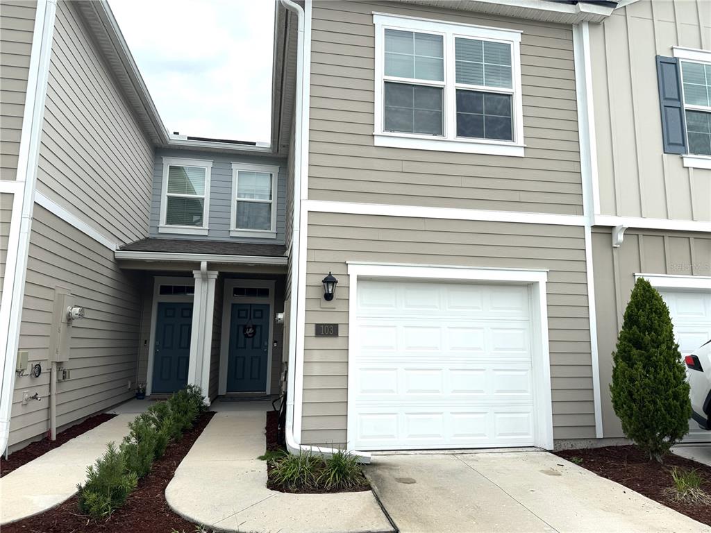 A two-story townhouse with beige siding, a single-car garage, and two front entry doors — 103 REDBUD ROAD, PALM COAST, FL