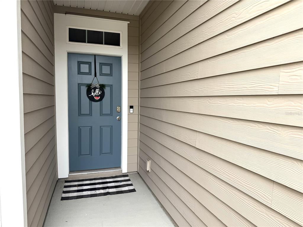 A blue front door with a welcome sign sits on a covered porch with siding — 103 REDBUD ROAD, PALM COAST, FL
