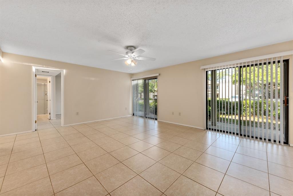 An empty living room with beige tile flooring, a ceiling fan, and two sliding glass doors — 2232 BAHIA VISTA STREET UNIT A1, SARASOTA, FL