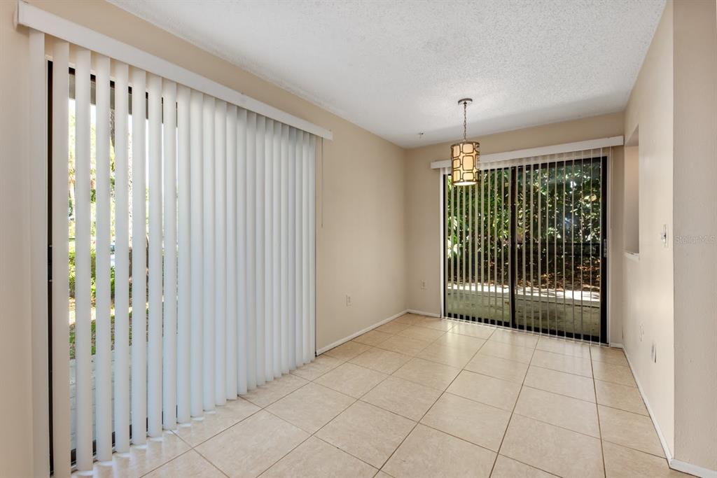 An empty dining room with beige tile floors, vertical blinds, and a hanging light fixture — 2232 BAHIA VISTA STREET UNIT A1, SARASOTA, FL