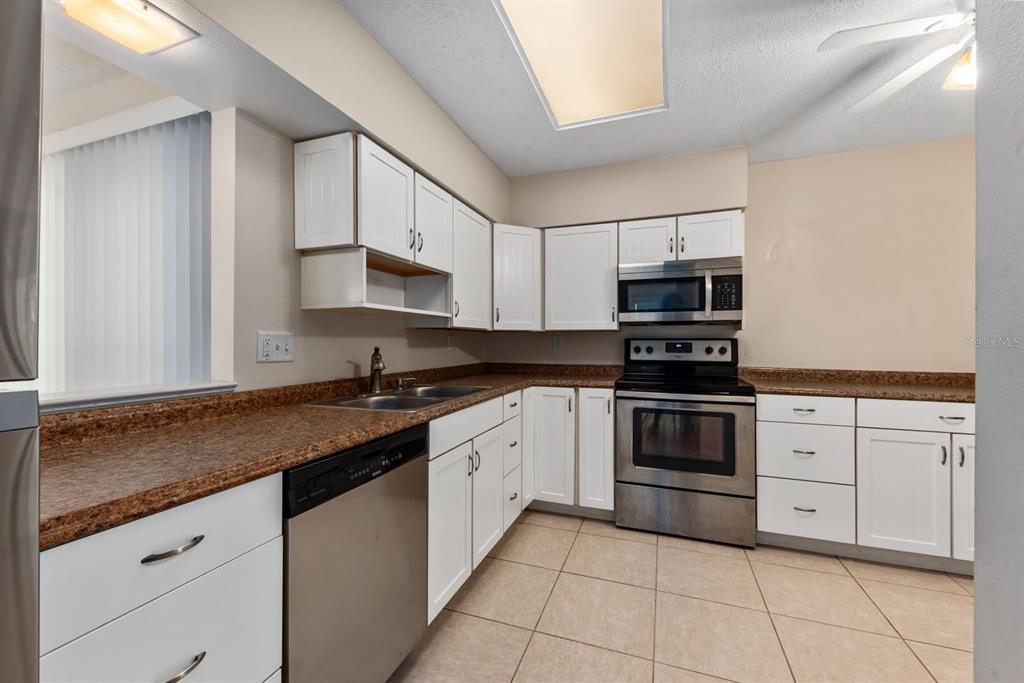 A kitchen features white cabinets, stainless steel appliances, and brown speckled laminate countertops — 2232 BAHIA VISTA STREET UNIT A1, SARASOTA, FL