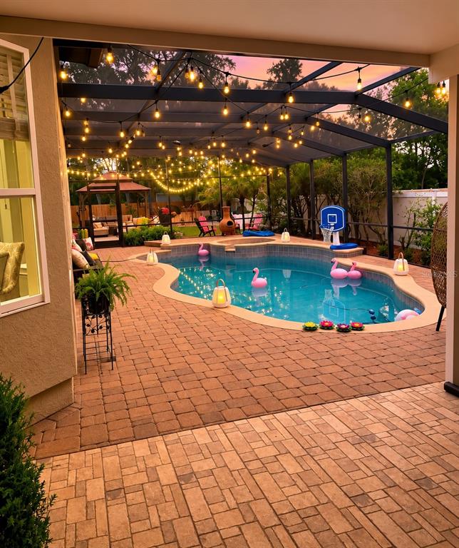 A screened-in patio features a pool with floating flamingo decor and overhead string lights — 6203 COURTNEY COVE, APOPKA, FL
