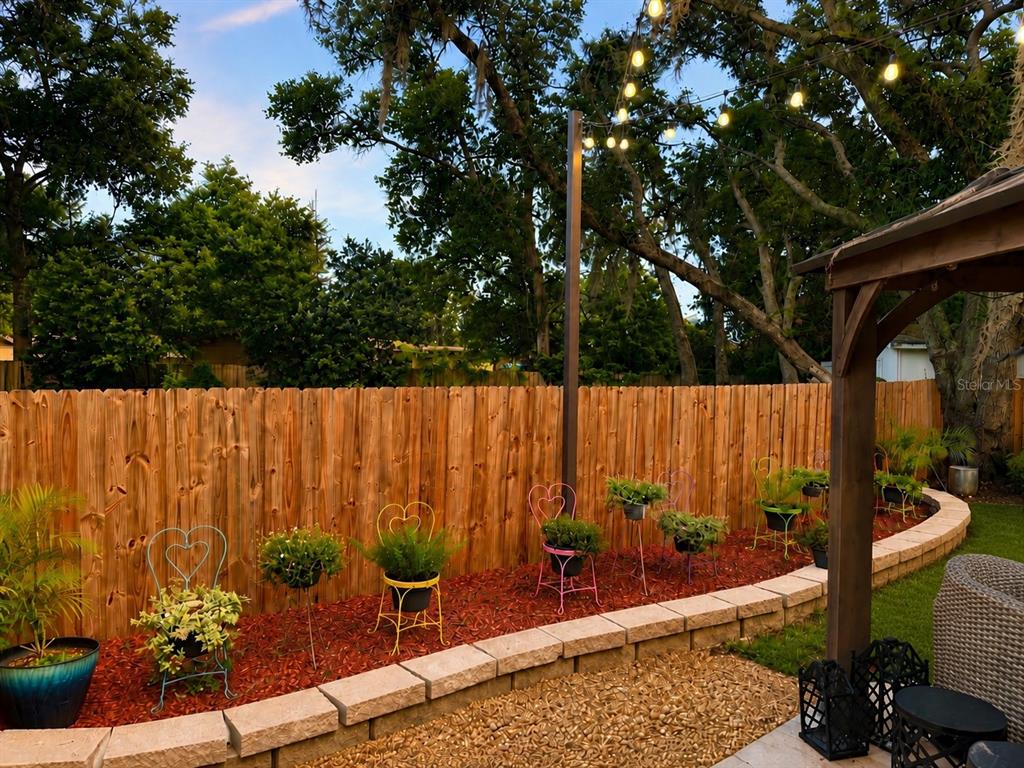 A backyard patio features a stone retaining wall, decorative metal chairs with plants, and string lights — 6203 COURTNEY COVE, APOPKA, FL