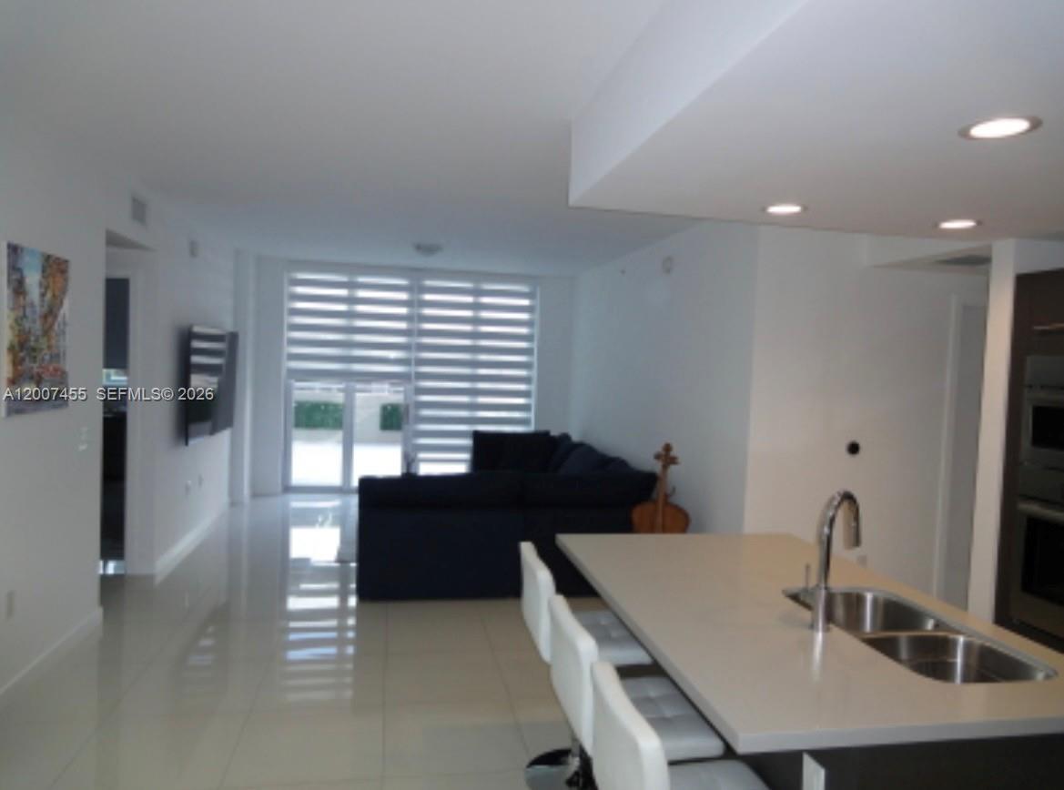 A modern kitchen with a quartz island and bar stools overlooks a living area — 7825 NW 107th Ave # 221, Doral FL 33178, DORAL, FL