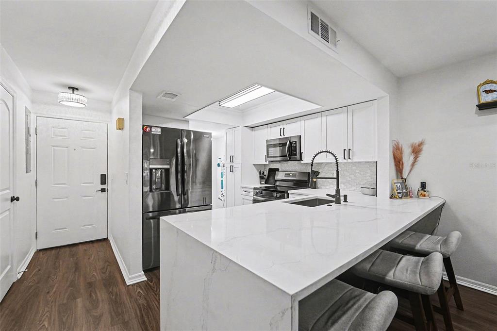A modern kitchen features white marble countertops, a breakfast bar, and stainless steel appliances — 5197 SILENT LOOP UNIT 121, NEW PORT RICHEY, FL