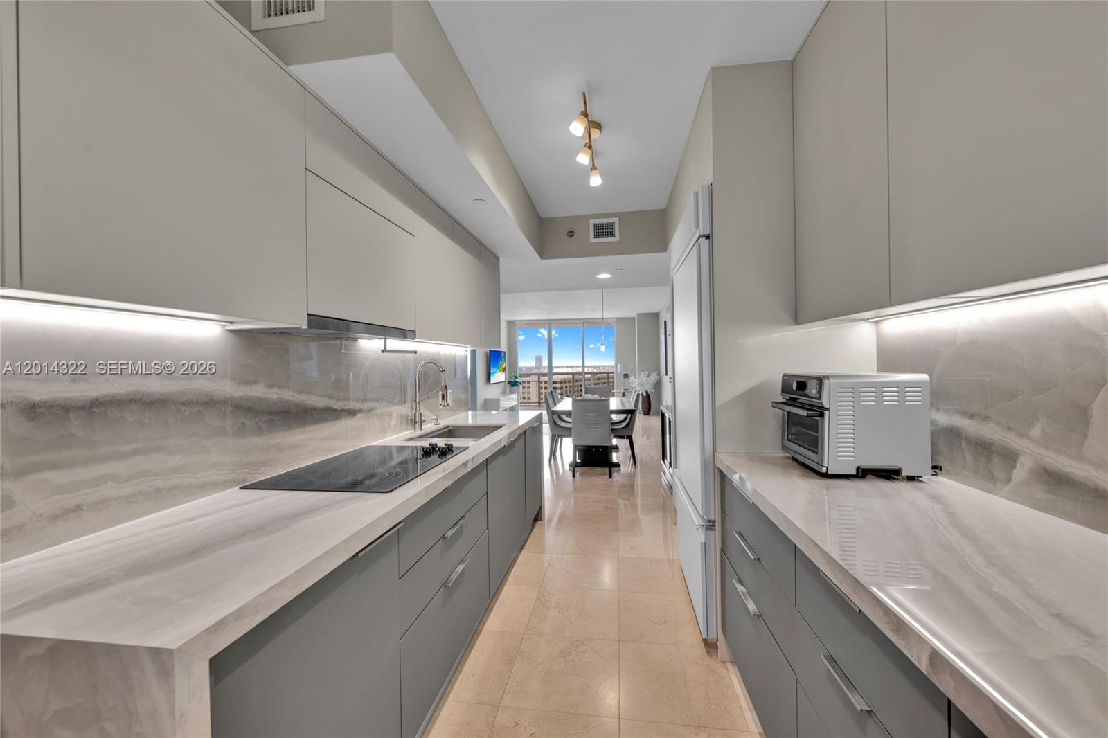 A modern galley kitchen features gray cabinetry, stone countertops, and a view of the dining area — 1800 S Ocean Dr # 2007, Hallandale Beach FL 33009, HALLANDALE BEACH, FL