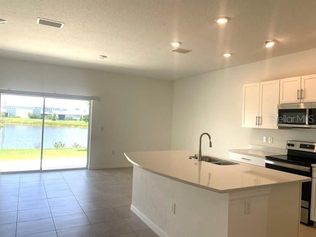 A kitchen with white cabinets and a quartz island overlooks a lake through sliding doors — 5730 ARCHIPELAGO, NOKOMIS, FL