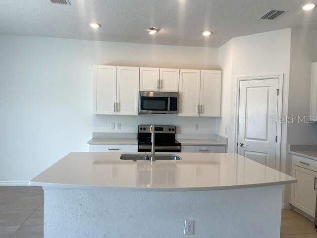 A kitchen features white cabinets, stainless steel appliances, and a large central island with a sink — 5730 ARCHIPELAGO, NOKOMIS, FL