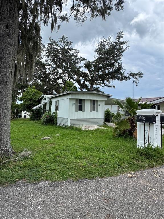 A white mobile home with a carport sits on a grassy lot under large trees — 39611 GLORYLAND DRIVE, DADE CITY, FL