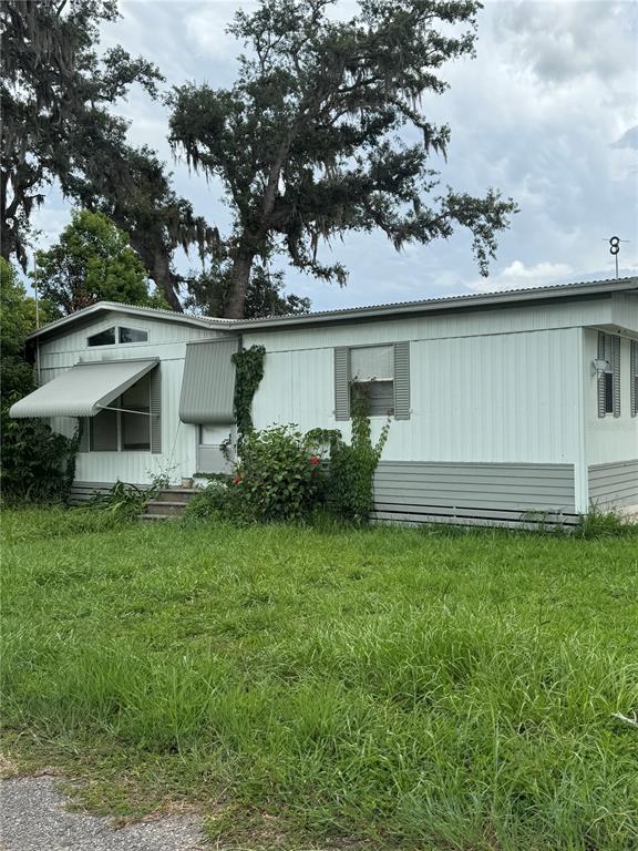 A single-story mobile home with light-colored siding, metal awnings, and overgrown grass in the yard — 39611 GLORYLAND DRIVE, DADE CITY, FL