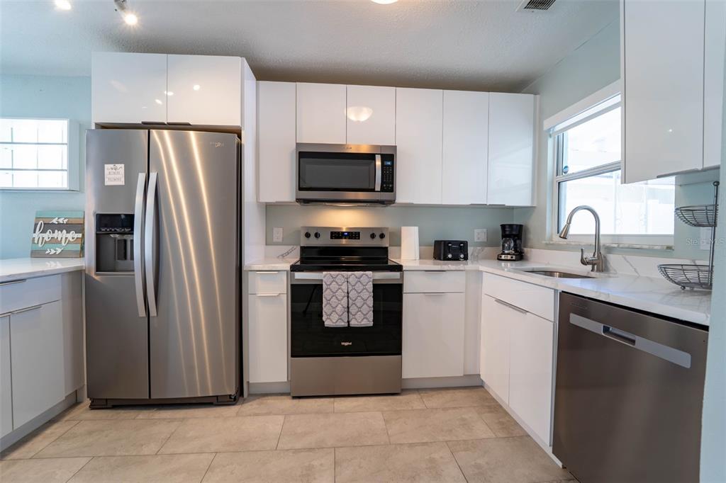 A modern kitchen features white cabinets, stainless steel appliances, and light-colored tile flooring — 4825 FLORAMAR TERRACE, NEW PORT RICHEY, FL