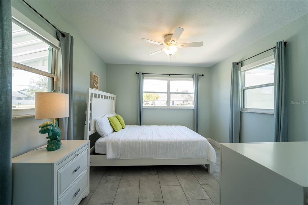 A bedroom with light green walls, a white bed, tile floors, and three windows — 4825 FLORAMAR TERRACE, NEW PORT RICHEY, FL