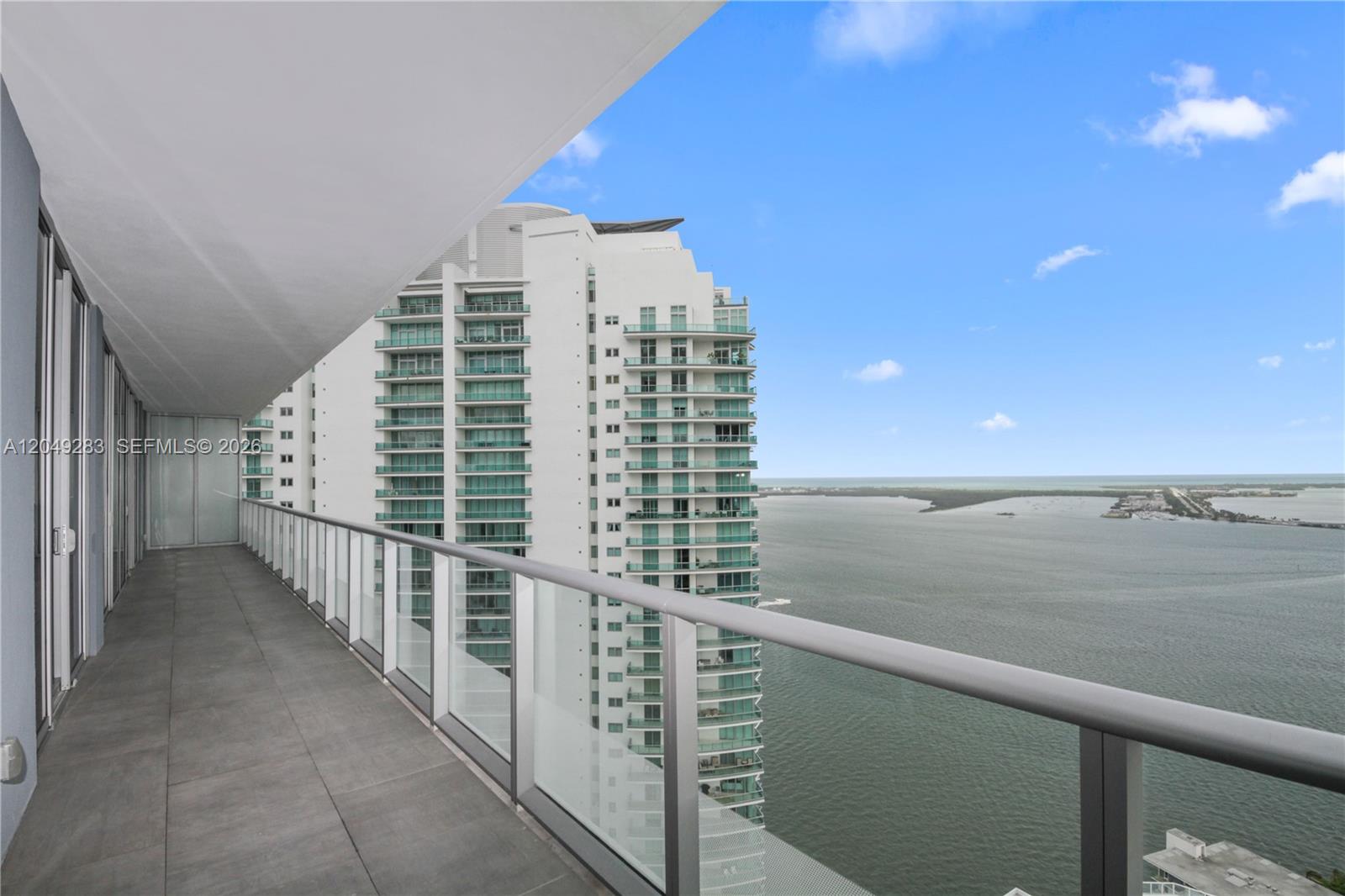 A high-rise balcony with glass railings overlooks a large body of water and buildings — 1300 Brickell Bay Dr # 4102, Miami FL 33131, MIAMI, FL