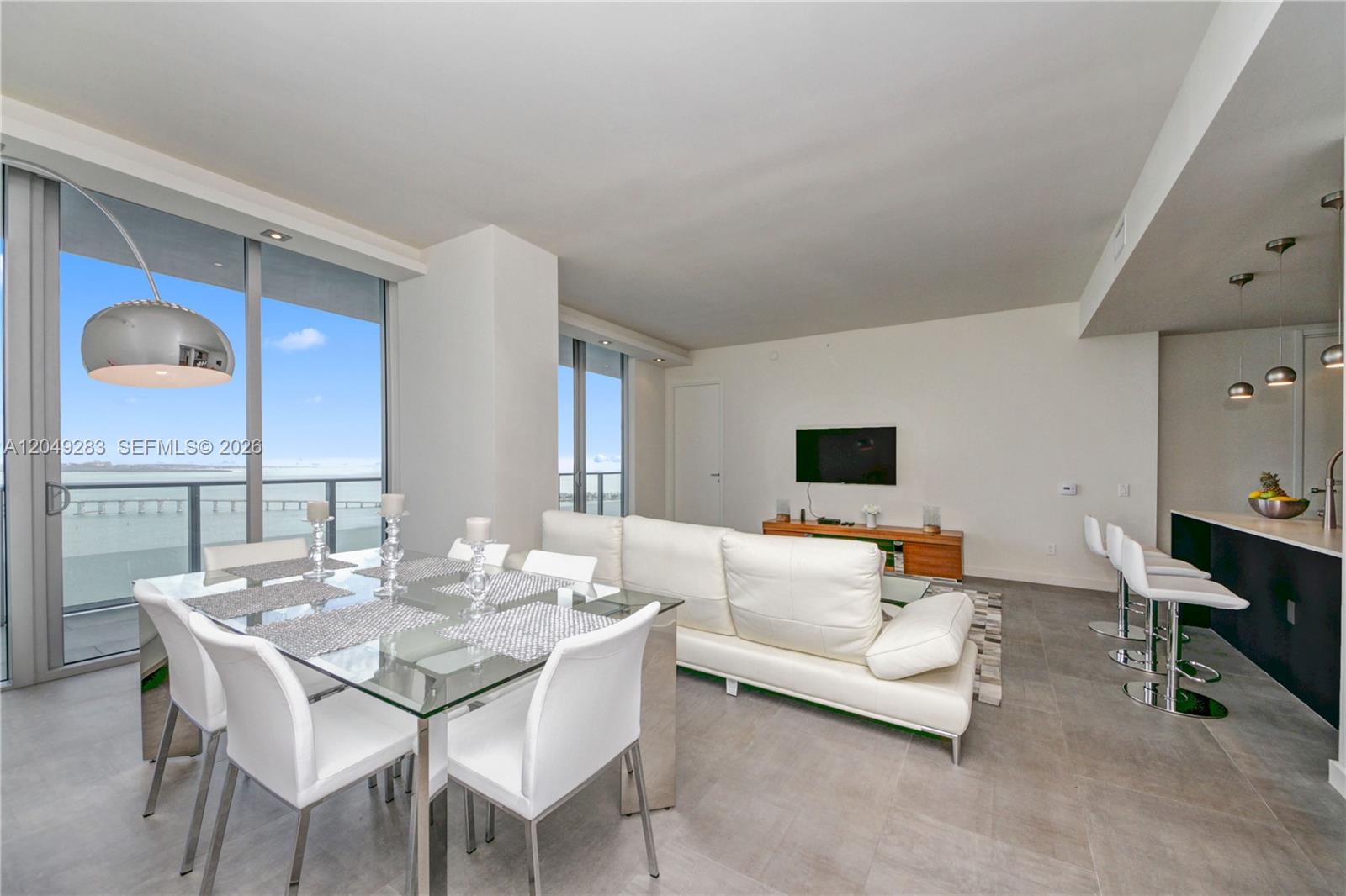 A modern living and dining area features white furniture, tile floors, and a balcony view — 1300 Brickell Bay Dr # 4102, Miami FL 33131, MIAMI, FL