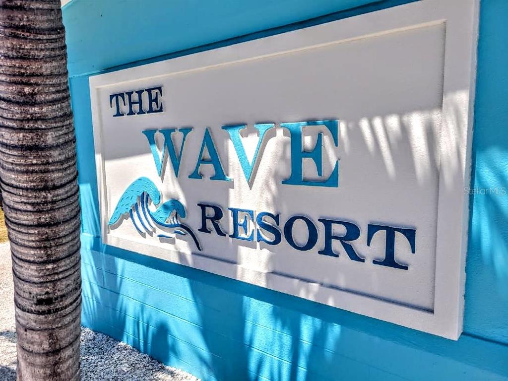 A sign for The Wave Resort is mounted on a bright blue exterior wall — 13343 GULF BOULEVARD UNIT C-12, MADEIRA BEACH, FL