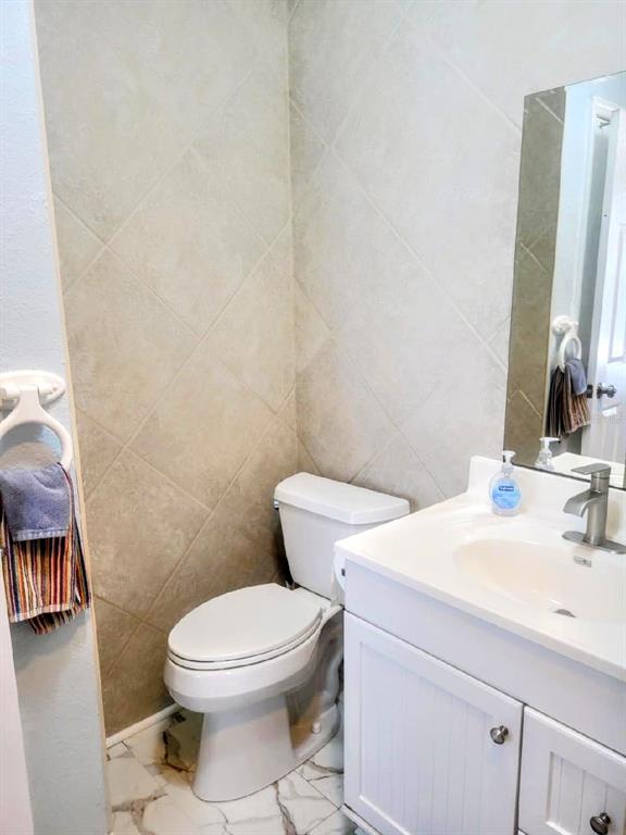 A bathroom features a white toilet, a vanity with a sink, and diagonal wall tiles — 13343 GULF BOULEVARD UNIT C-12, MADEIRA BEACH, FL