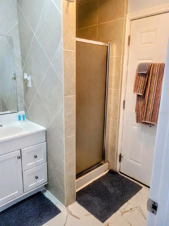 A bathroom features a white vanity, a tiled shower stall, and a door with towels — 13343 GULF BOULEVARD UNIT C-12, MADEIRA BEACH, FL
