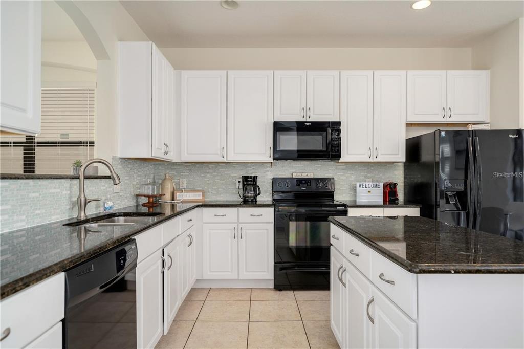 A kitchen features white cabinets, dark granite countertops, black appliances, and a light-colored tile floor — 2641 TRANQUILITY WAY, KISSIMMEE, FL