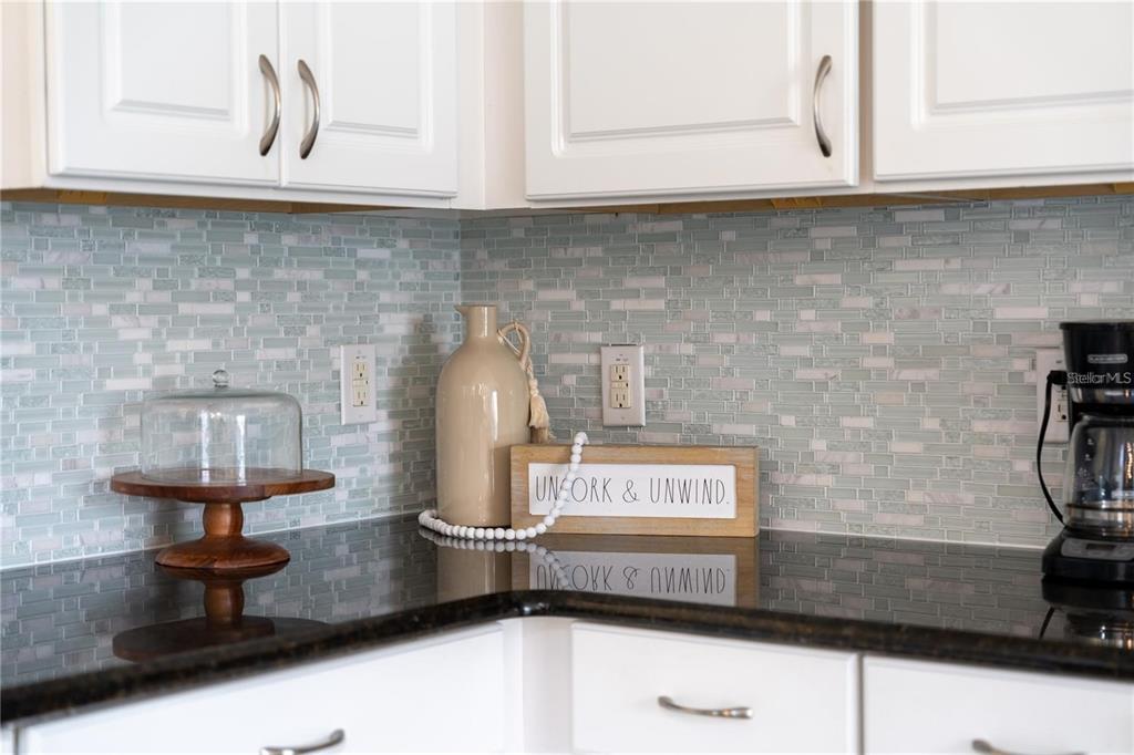 A kitchen corner features white cabinets, a light blue glass tile backsplash, and dark countertops — 2641 TRANQUILITY WAY, KISSIMMEE, FL