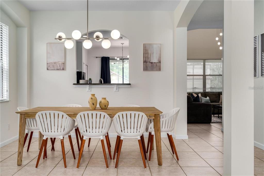 A dining room features a wooden table, white chairs, and a modern globe light fixture — 2641 TRANQUILITY WAY, KISSIMMEE, FL