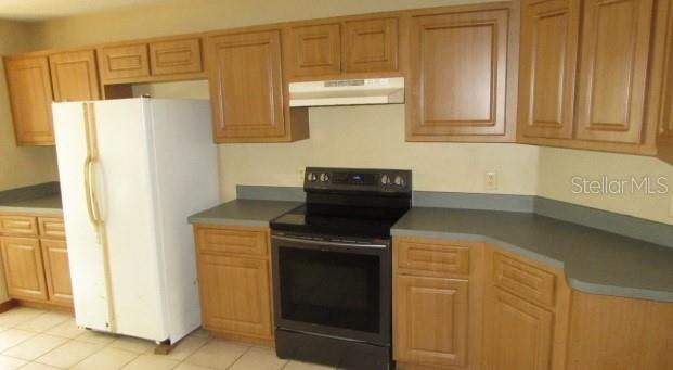 A kitchen features light wood cabinets, a white refrigerator, and a black electric stove — 824 BERRYHILL CIRCLE, FRUITLAND PARK, FL