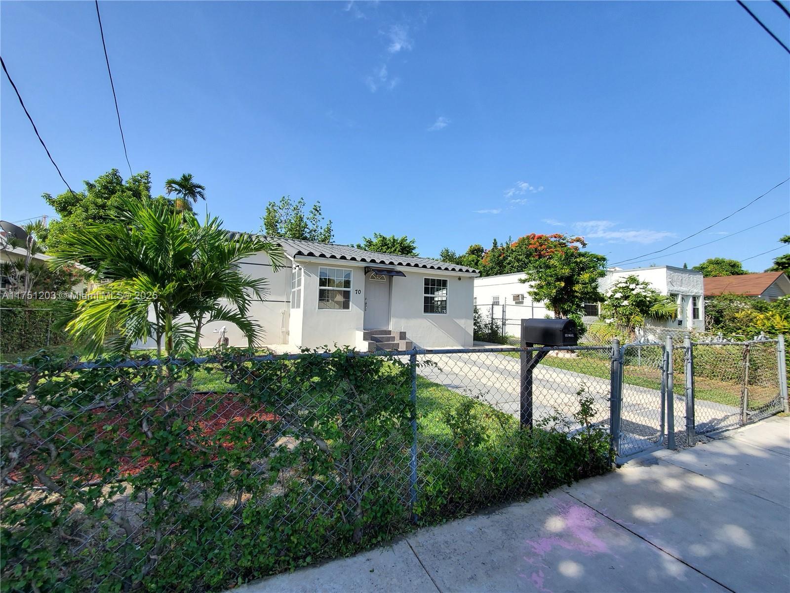 A single-story white house with a tiled roof sits behind a chain-link fence — 70 NW 33rd St, Miami FL 33127, MIAMI, FL