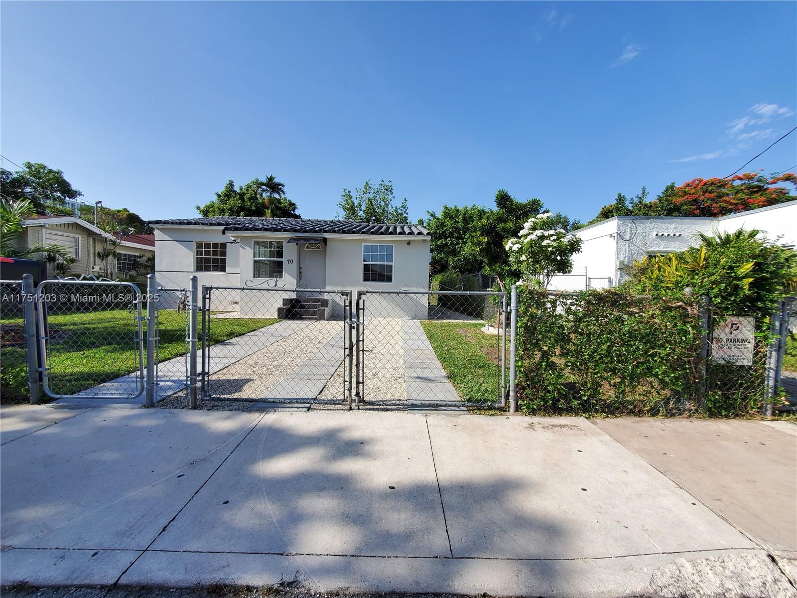 A single-story house with a gravel driveway and chain-link fence sits under a blue sky — 70 NW 33rd St, Miami FL 33127, MIAMI, FL