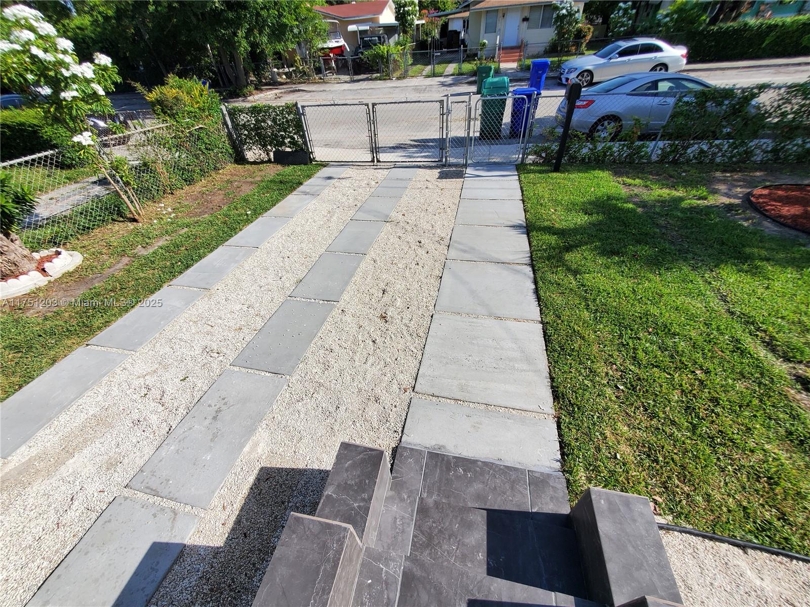 A paved walkway and gravel driveway lead to a gated entrance in a residential yard — 70 NW 33rd St, Miami FL 33127, MIAMI, FL