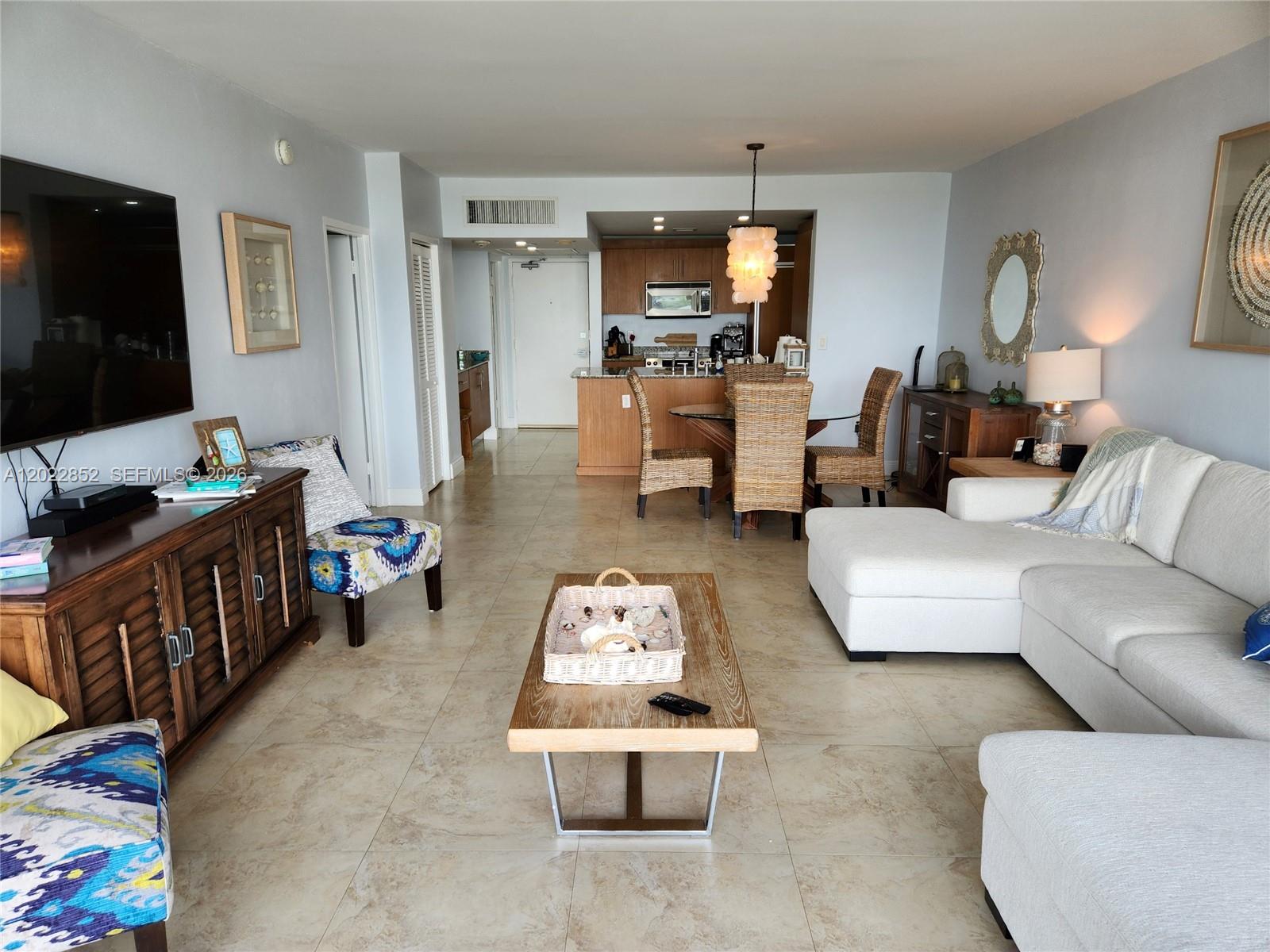An open-concept living and dining area features tile flooring, a sectional sofa, and kitchen cabinetry — 10275 Collins Ave # 824, Bal Harbour FL 33154, BAL HARBOUR, FL