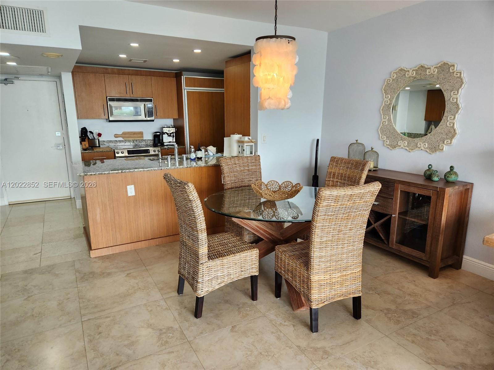 A dining area with a glass table and wicker chairs sits beside a wooden kitchen — 10275 Collins Ave # 824, Bal Harbour FL 33154, BAL HARBOUR, FL