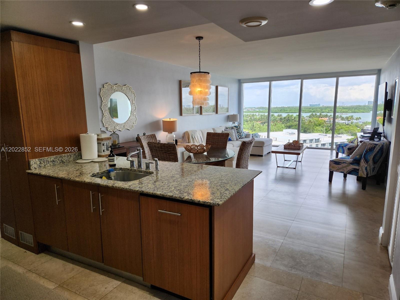 A kitchen with granite countertops and wood cabinets overlooks a living area with floor-to-ceiling windows — 10275 Collins Ave # 824, Bal Harbour FL 33154, BAL HARBOUR, FL