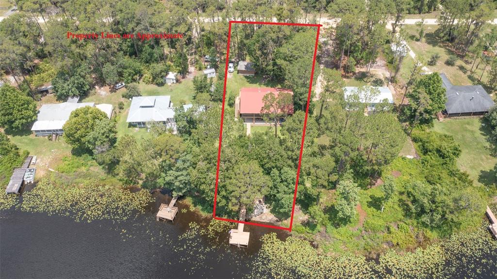 An aerial view shows a house with a red roof situated on a wooded waterfront lot — 303 RILEY LAKE DRIVE, HAWTHORNE, FL