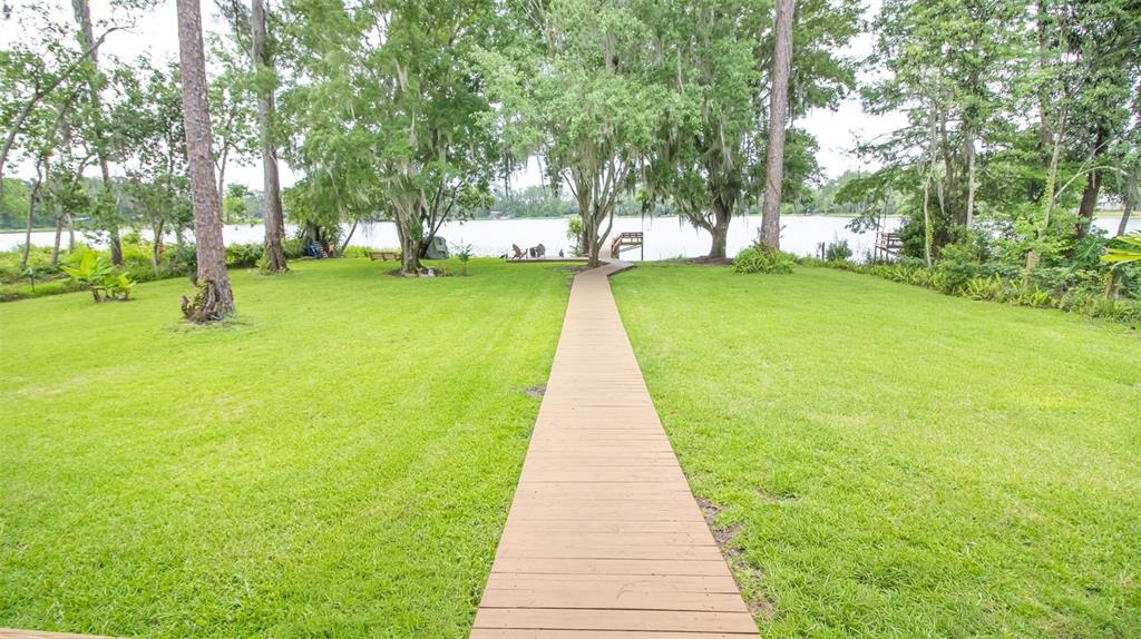 A wooden walkway leads through a grassy lawn toward a lake with trees — 303 RILEY LAKE DRIVE, HAWTHORNE, FL
