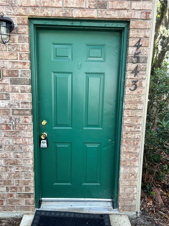 A green six-panel front door is set into a brick exterior wall — 4543 SW 44TH LANE, GAINESVILLE, FL