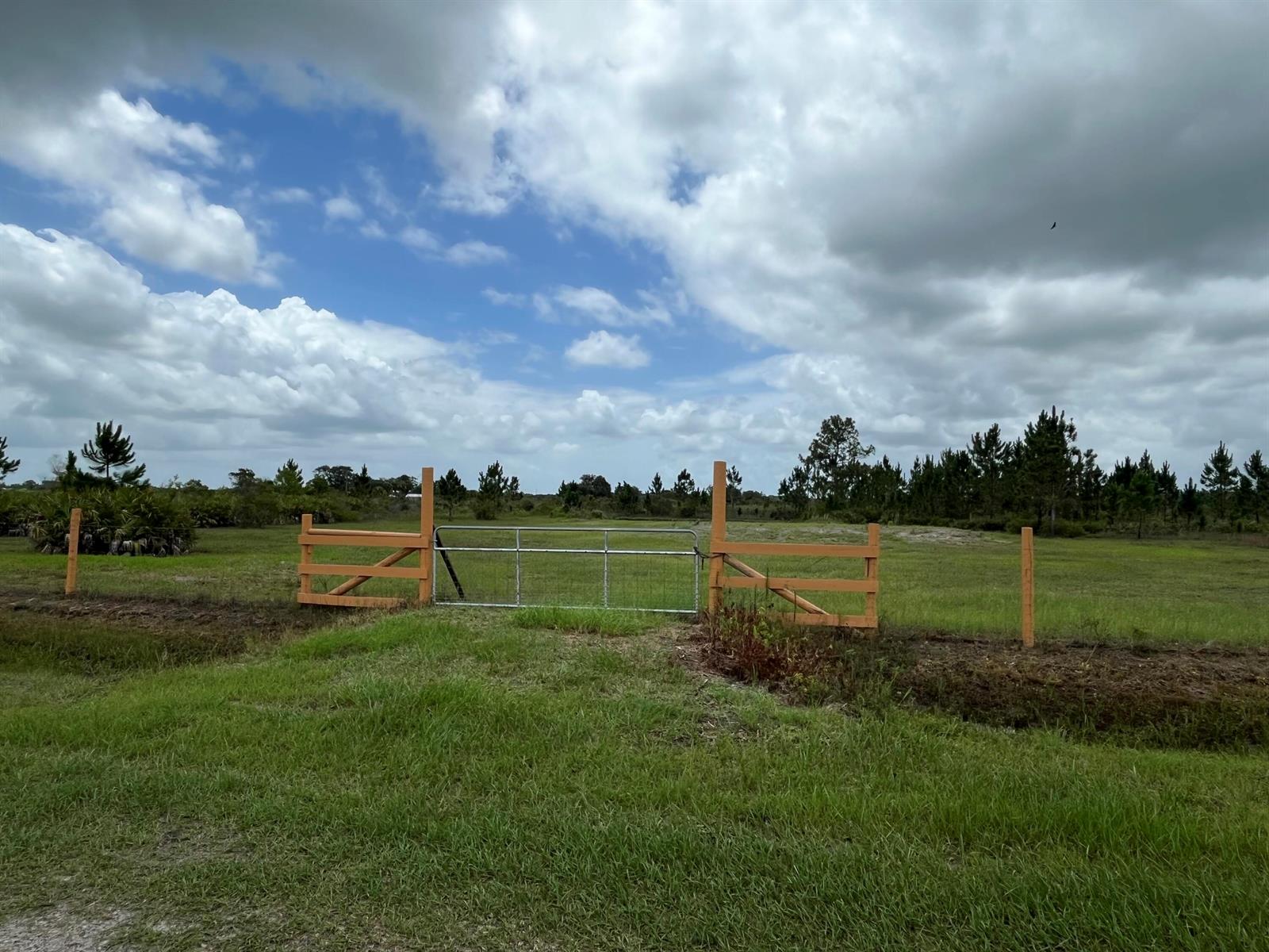 A metal gate set within a wooden fence on a grassy field under a cloudy sky — 19092 NW 250th Street, Okeechobee FL 34972, OKEECHOBEE, FL