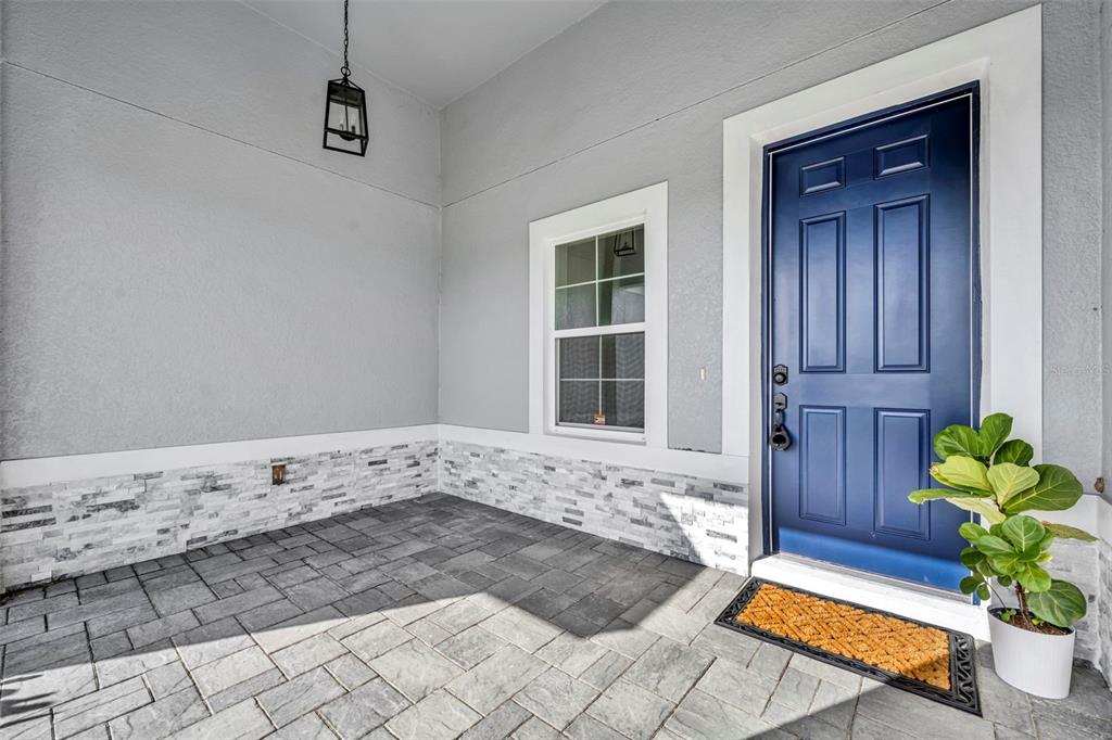 A front porch with gray stone veneer, paver flooring, and a blue front door — 49 ORCHID COURT, POINCIANA, FL