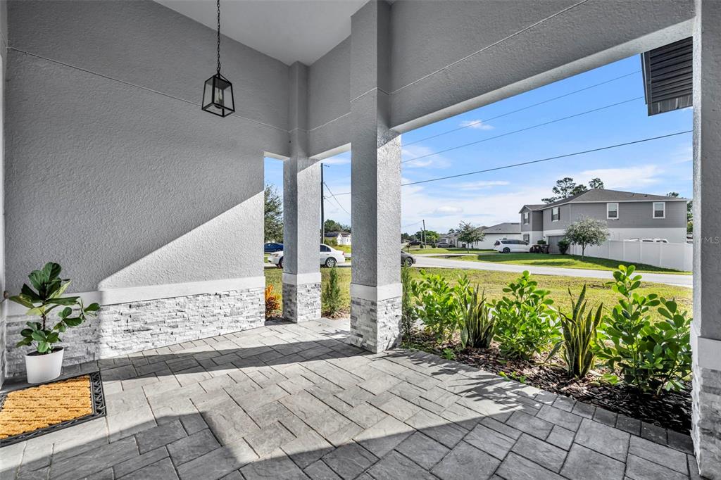 A covered front porch features stone-accented columns, gray paver flooring, and potted plants — 49 ORCHID COURT, POINCIANA, FL