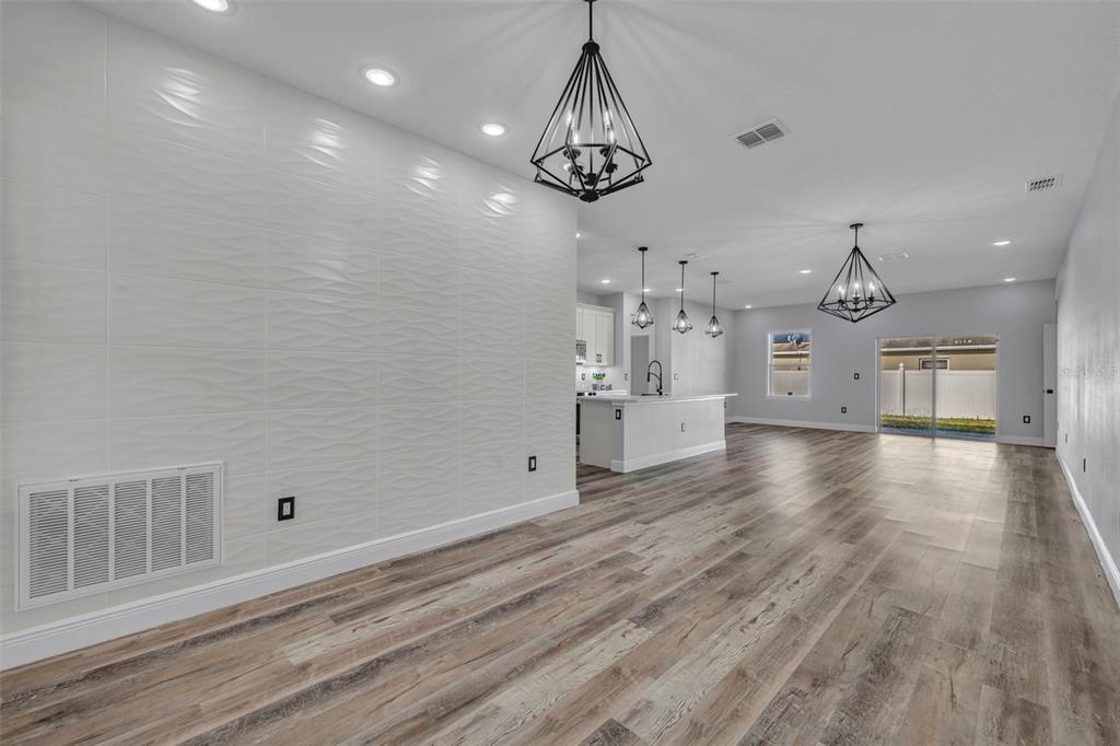A spacious open-concept living and kitchen area features wood-look flooring and a textured accent wall — 49 ORCHID COURT, POINCIANA, FL