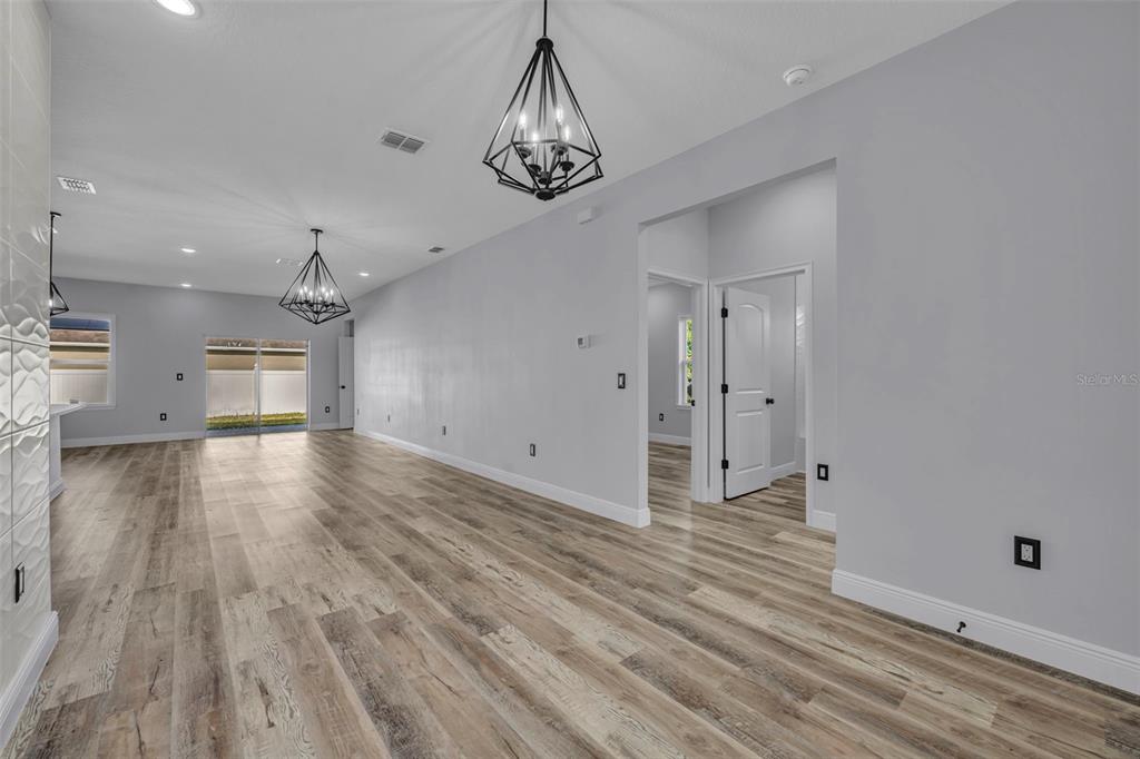 A spacious living area with light gray walls, wood-look flooring, and two geometric pendant lights — 49 ORCHID COURT, POINCIANA, FL