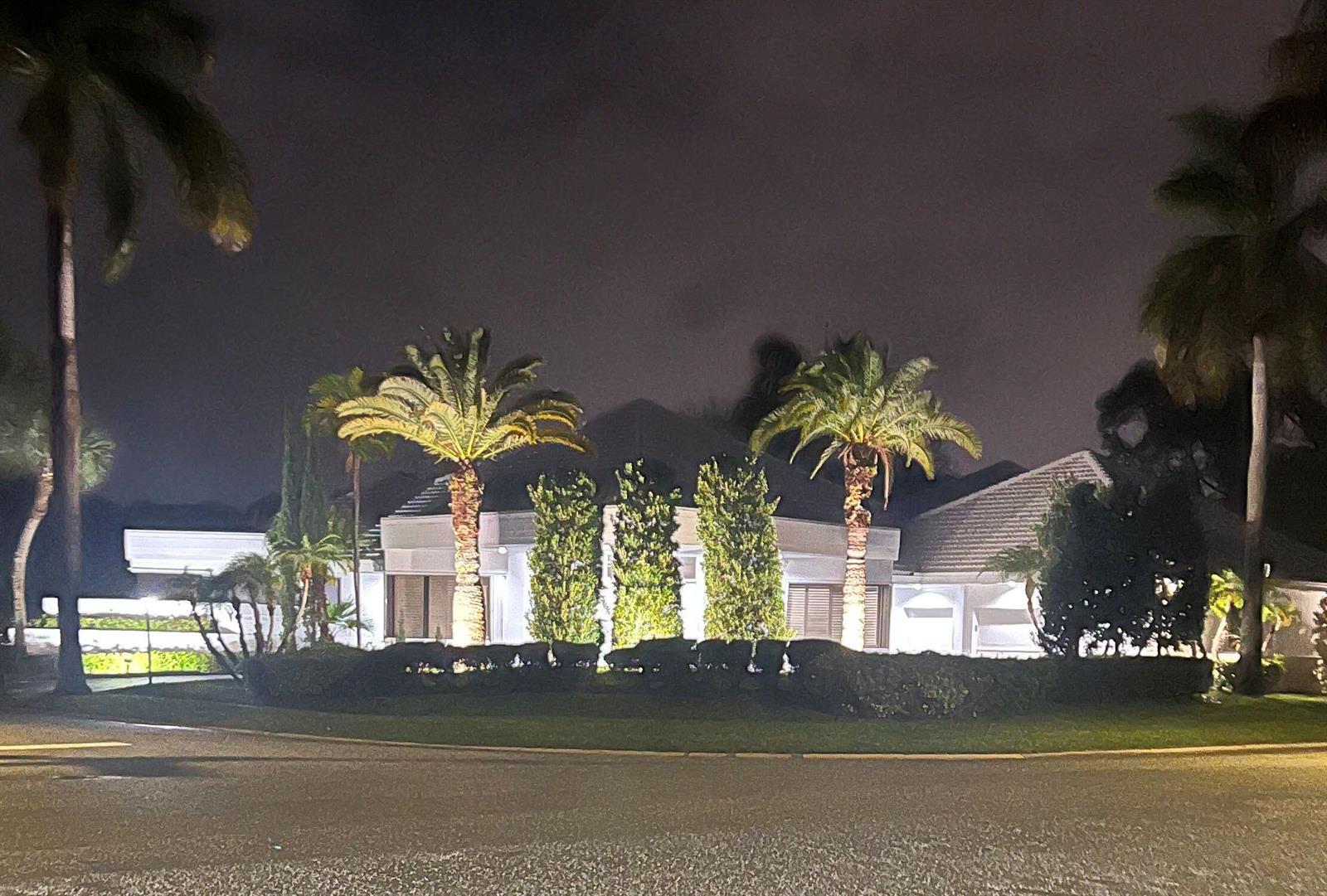 A night view of a single-story house exterior featuring illuminated palm trees and landscaping — 7215 Ballantrae Court, Boca Raton FL 33496, BOCA RATON, FL