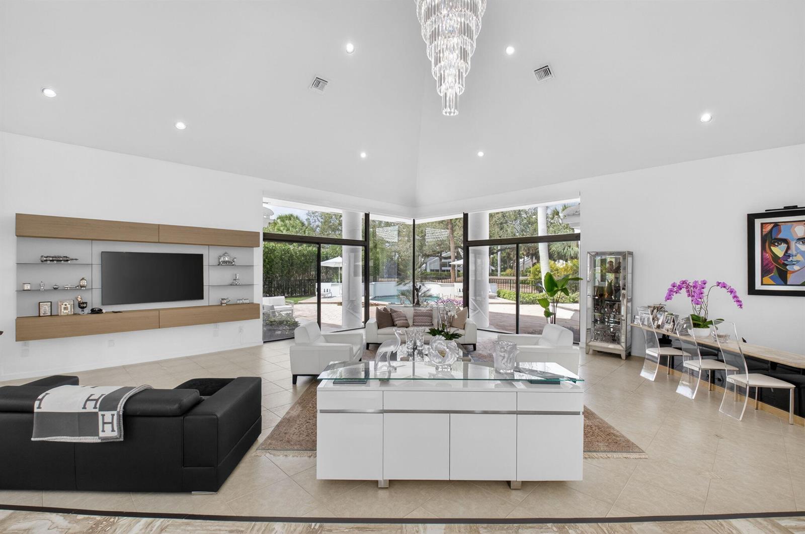 A spacious living room features a vaulted ceiling, large glass walls, and modern white furniture — 7215 Ballantrae Court, Boca Raton FL 33496, BOCA RATON, FL