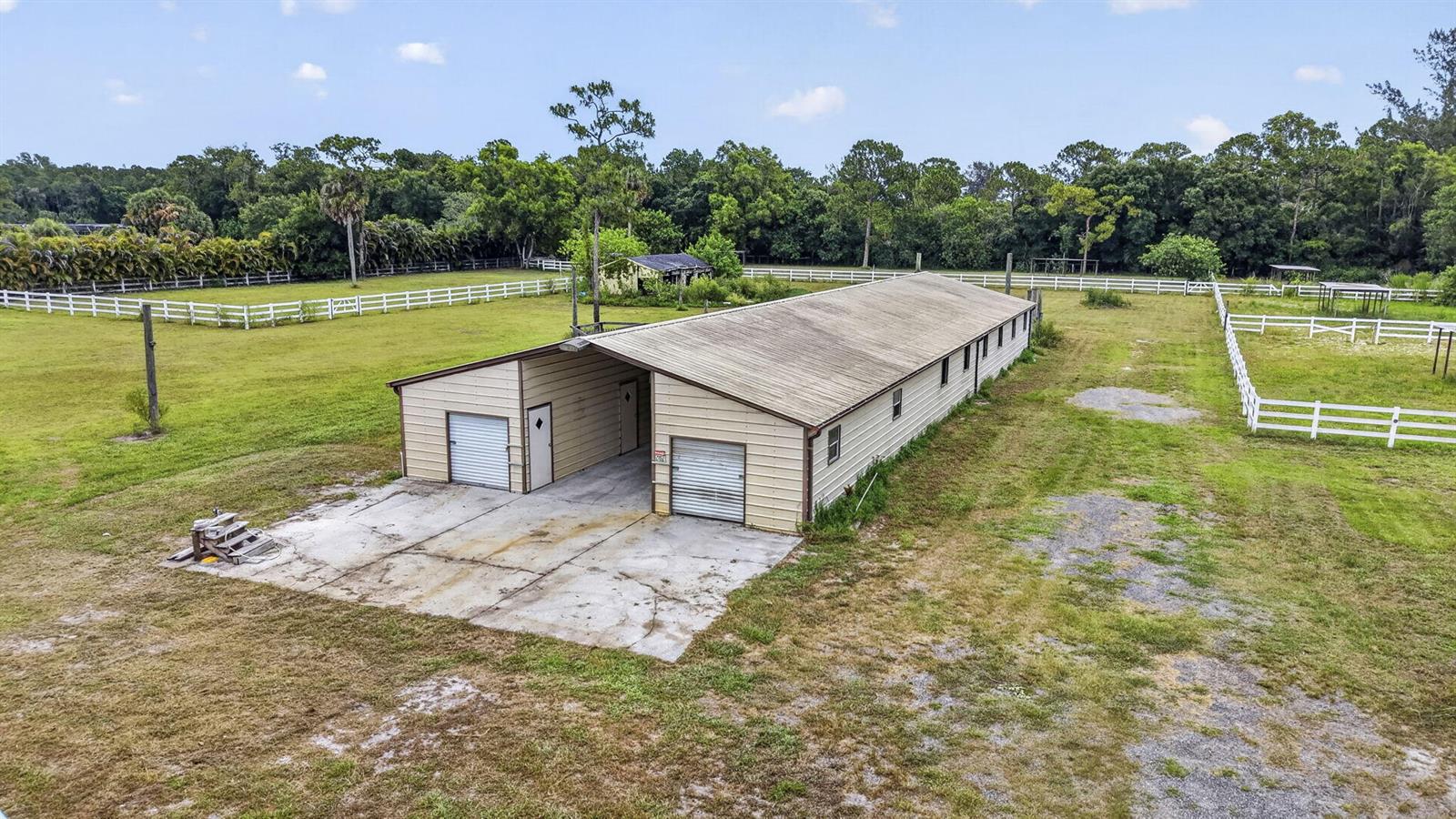 An aerial view shows a long, tan metal building with two garage doors and fenced pastures — 2944 A Road, Loxahatchee FL 33470, LOXAHATCHEE, FL